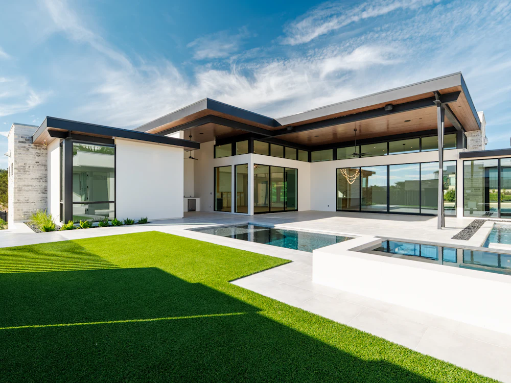 Pool with a wide lawn and paved surrounds beside a modern home