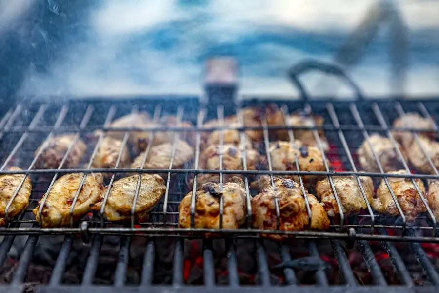 Marinated chicken pieces grilling in a basket over charcoal