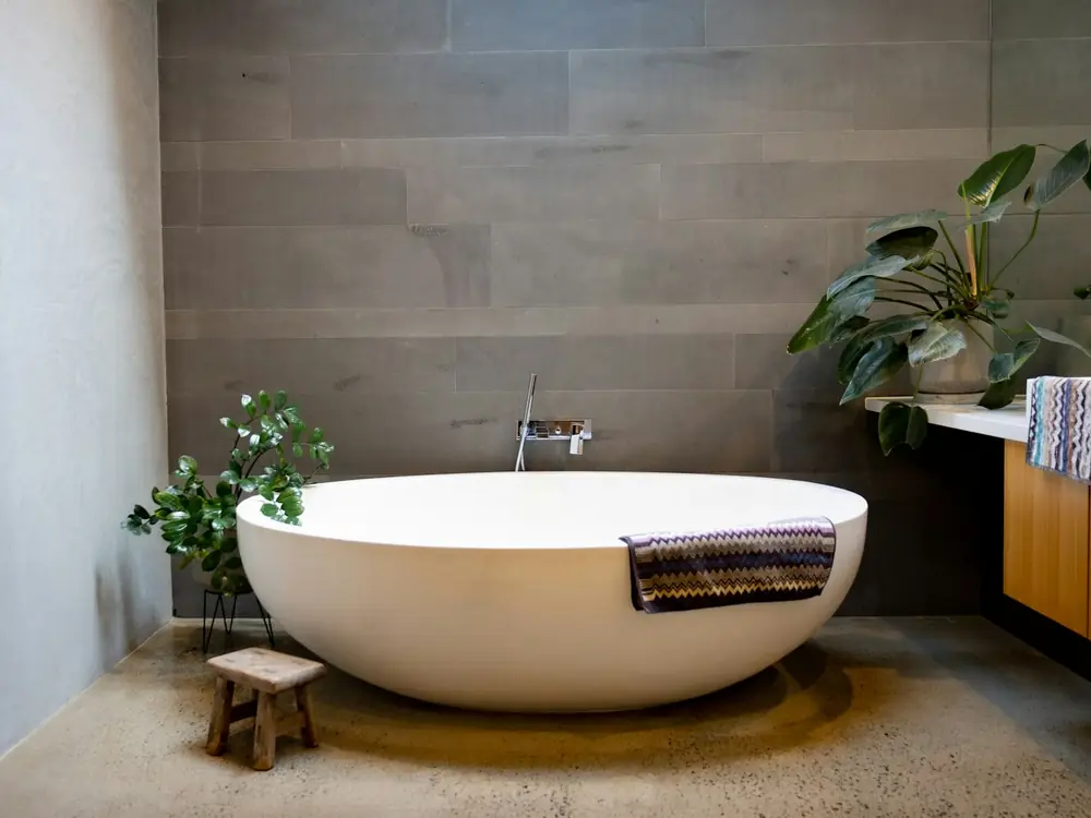 Freestanding stone bath on a polished concrete floor with a wall-mounted spout