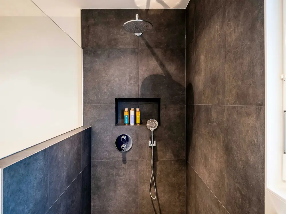 Walk-in shower with large-format dark tiles, niche and matte black mixer