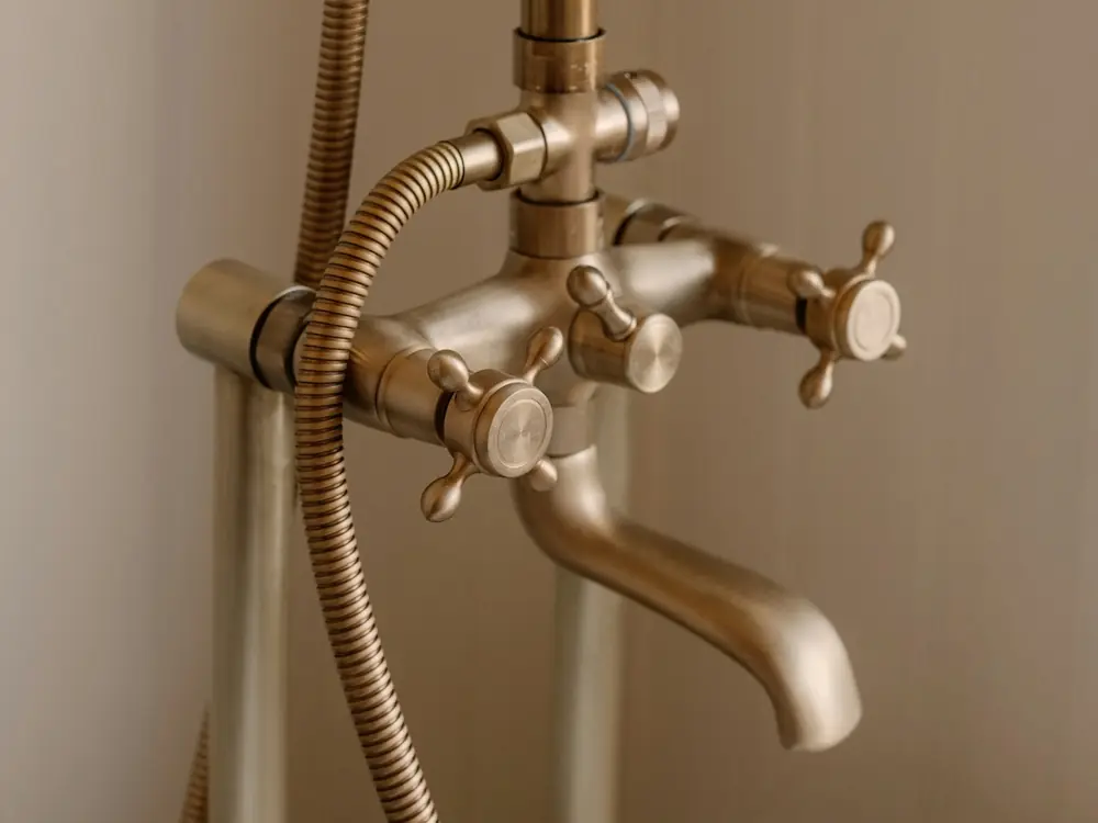 Brushed brass exposed bath mixer and shower set, installed level against a warm plaster wall