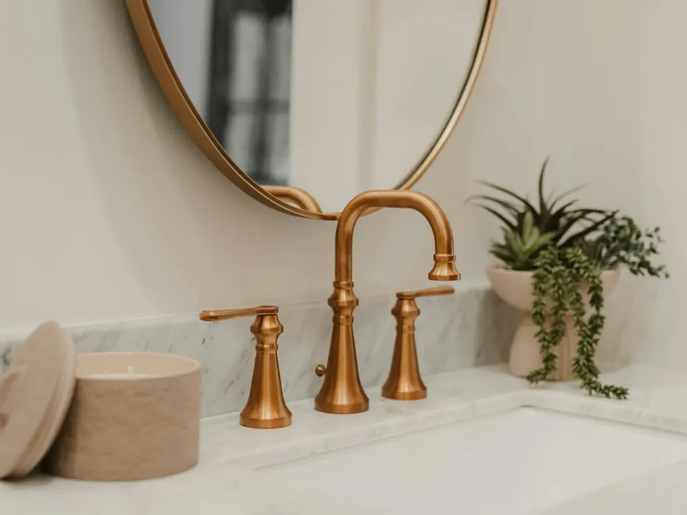 Brushed brass basin set with cross handles in front of a round brass mirror