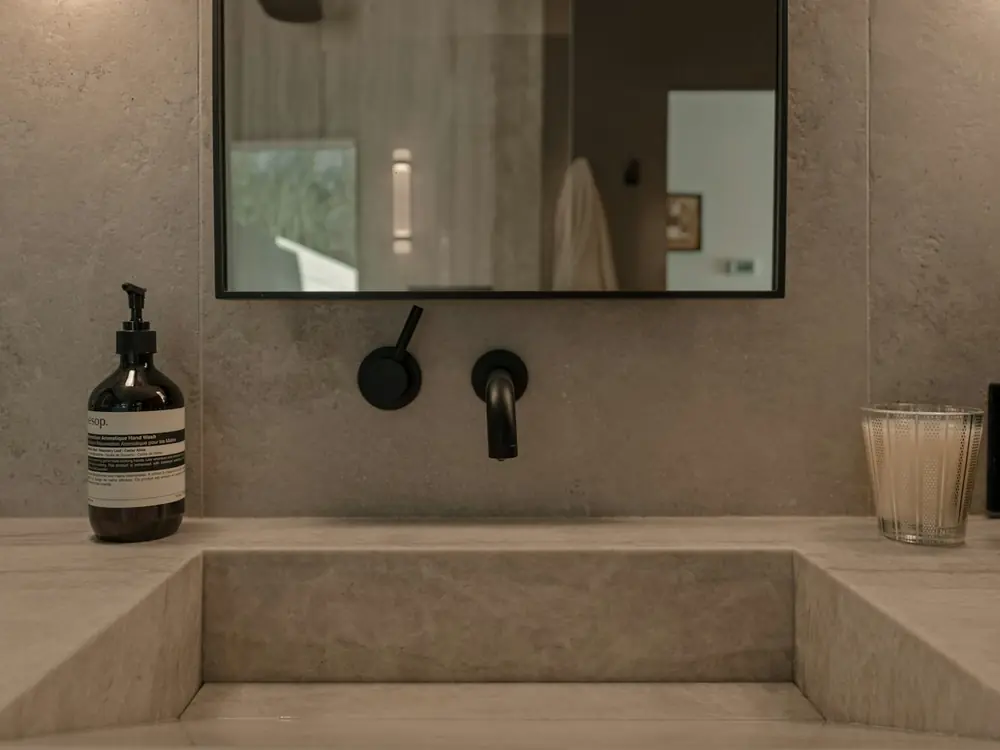 Matte black wall-mounted basin mixer over a stone trough basin