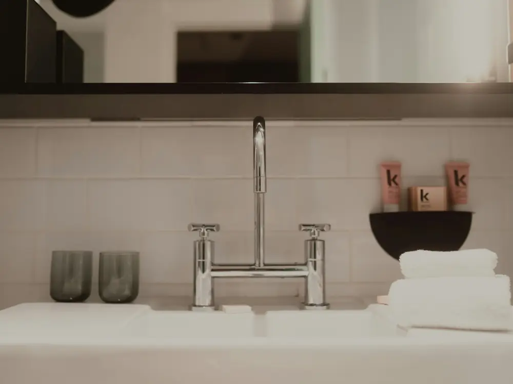 Chrome bridge-style basin mixer against white tiles