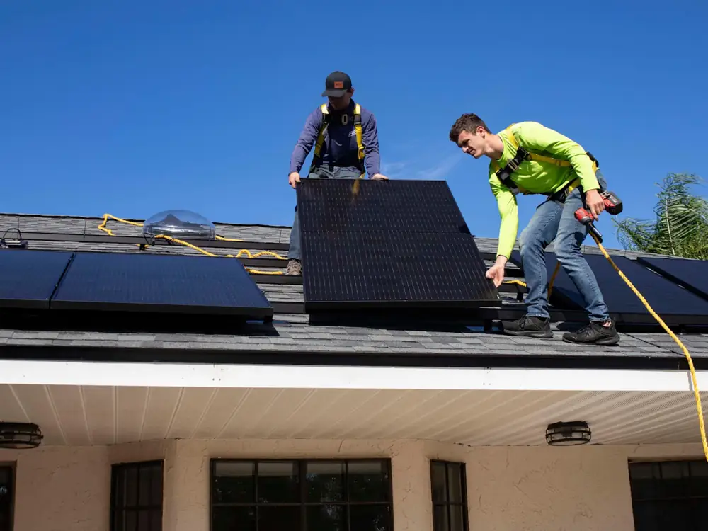 Two electricians fitting solar panels on a roof