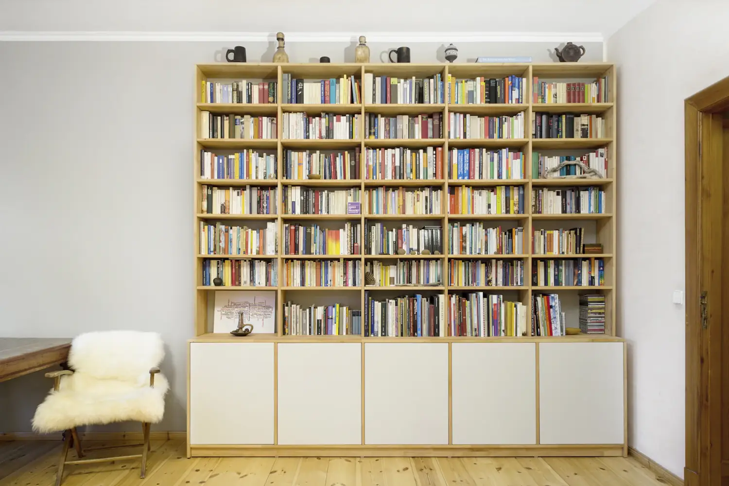 Floor-to-ceiling timber bookcase with white cupboards below, made to fit the wall