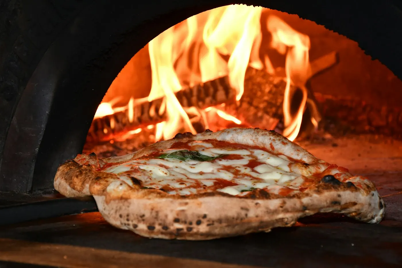 A margherita pizza puffing up next to the flames of a woodfired oven