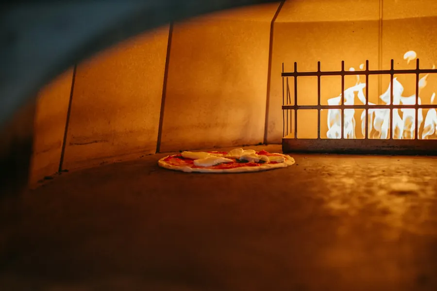 A pizza turning in the oven next to the flames