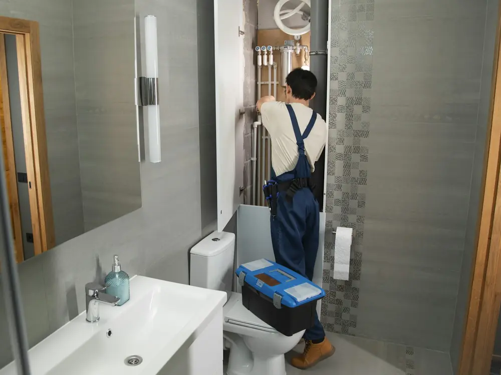 Plumber working on the pipework behind a bathroom wall panel