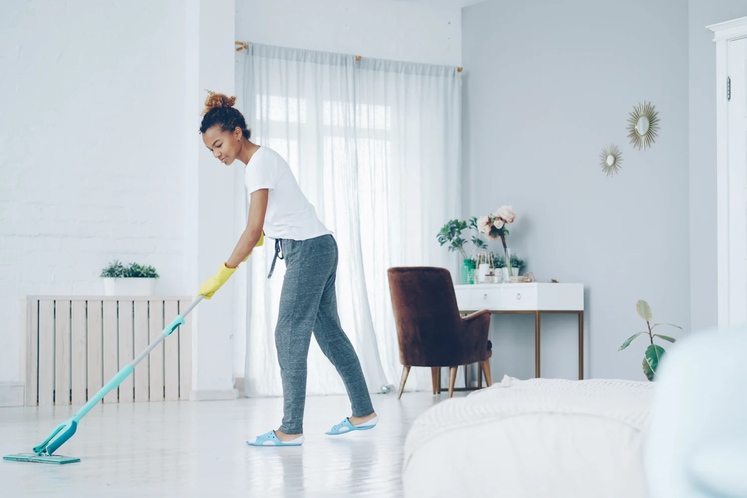 A Fresh Nest cleaner mopping a bright white bedroom floor