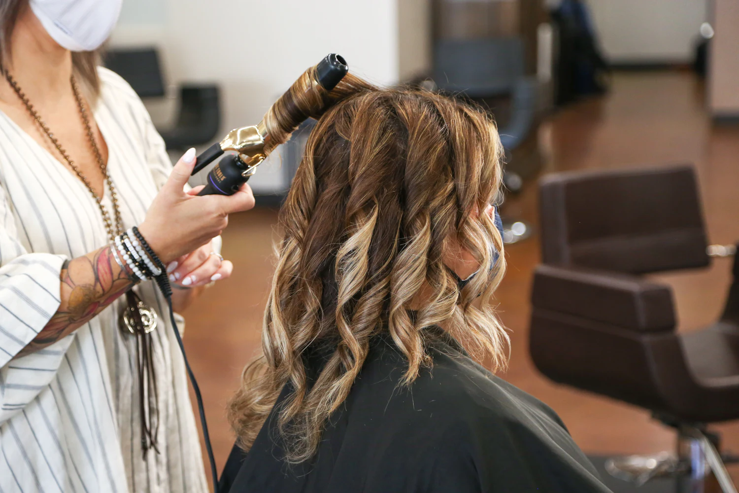 Stylist curling a client's highlighted hair with a curling iron