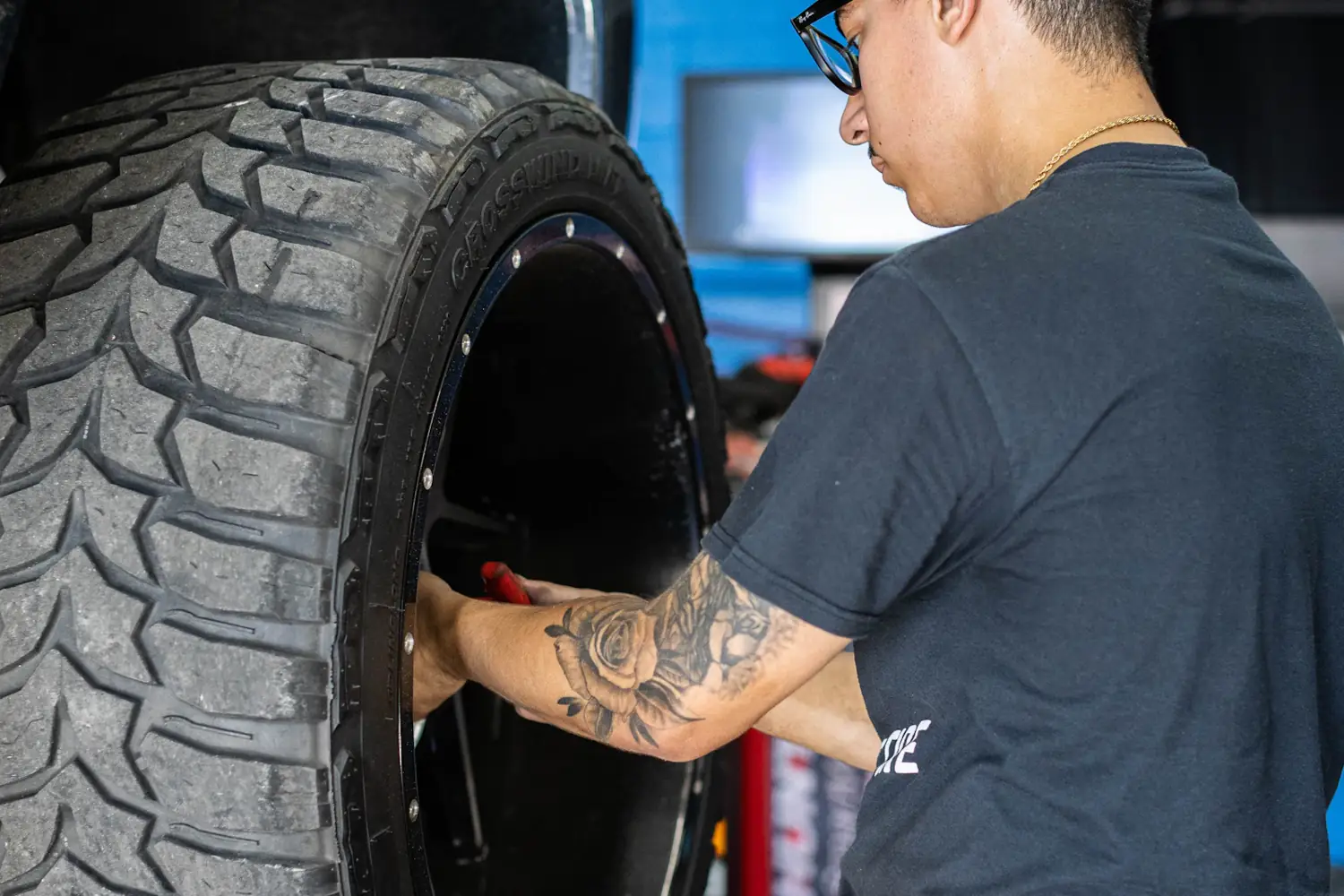 A tyre fitter mounting a new mud-terrain tyre on a black wheel in the workshop