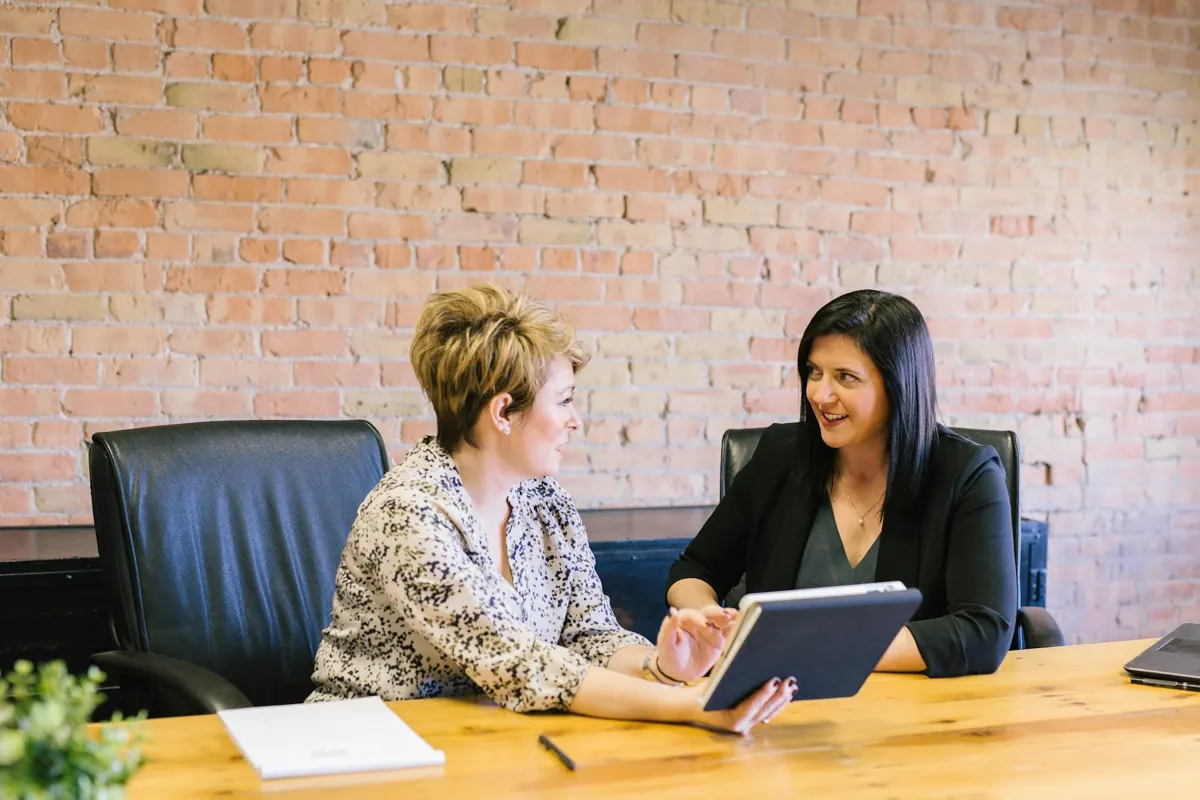 Two women at a meeting table going through a report on a tablet