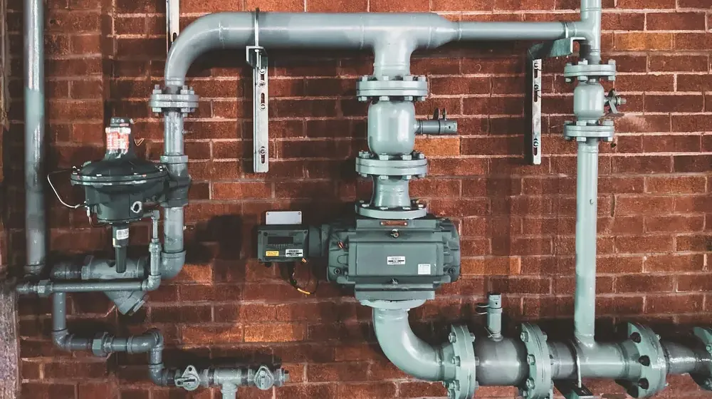 Gas-fired hot water plant pipework with regulator and meter on a brick plant room wall
