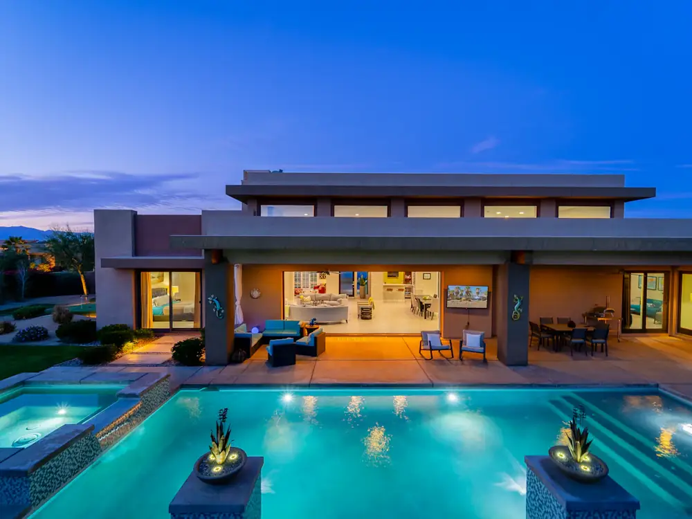 Custom home at dusk with an open living room facing a lit pool