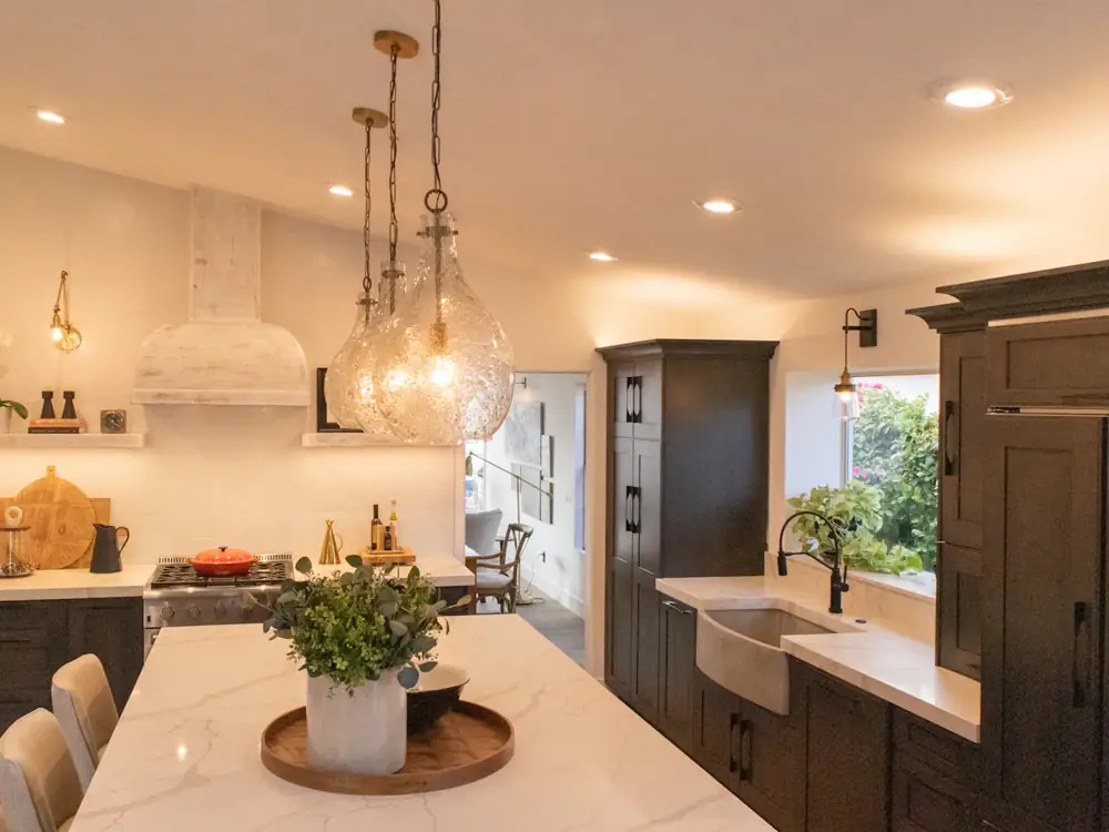 Renovated kitchen with a stone island, glass pendants and dark cabinetry