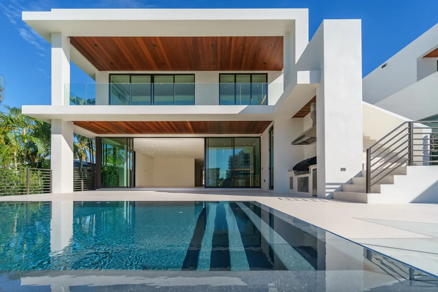 Two-storey white custom home with a timber-lined balcony and a long lap pool