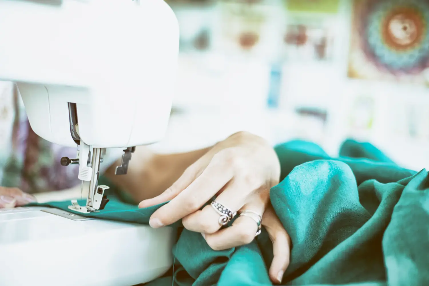 Hands guiding teal fabric under a sewing machine foot