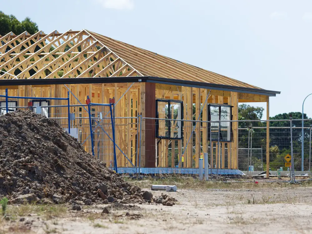 A new house frame on a building site with a mound of soil in front