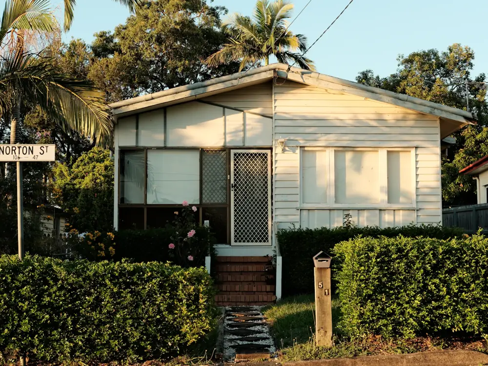 Small white weatherboard granny flat behind a hedge