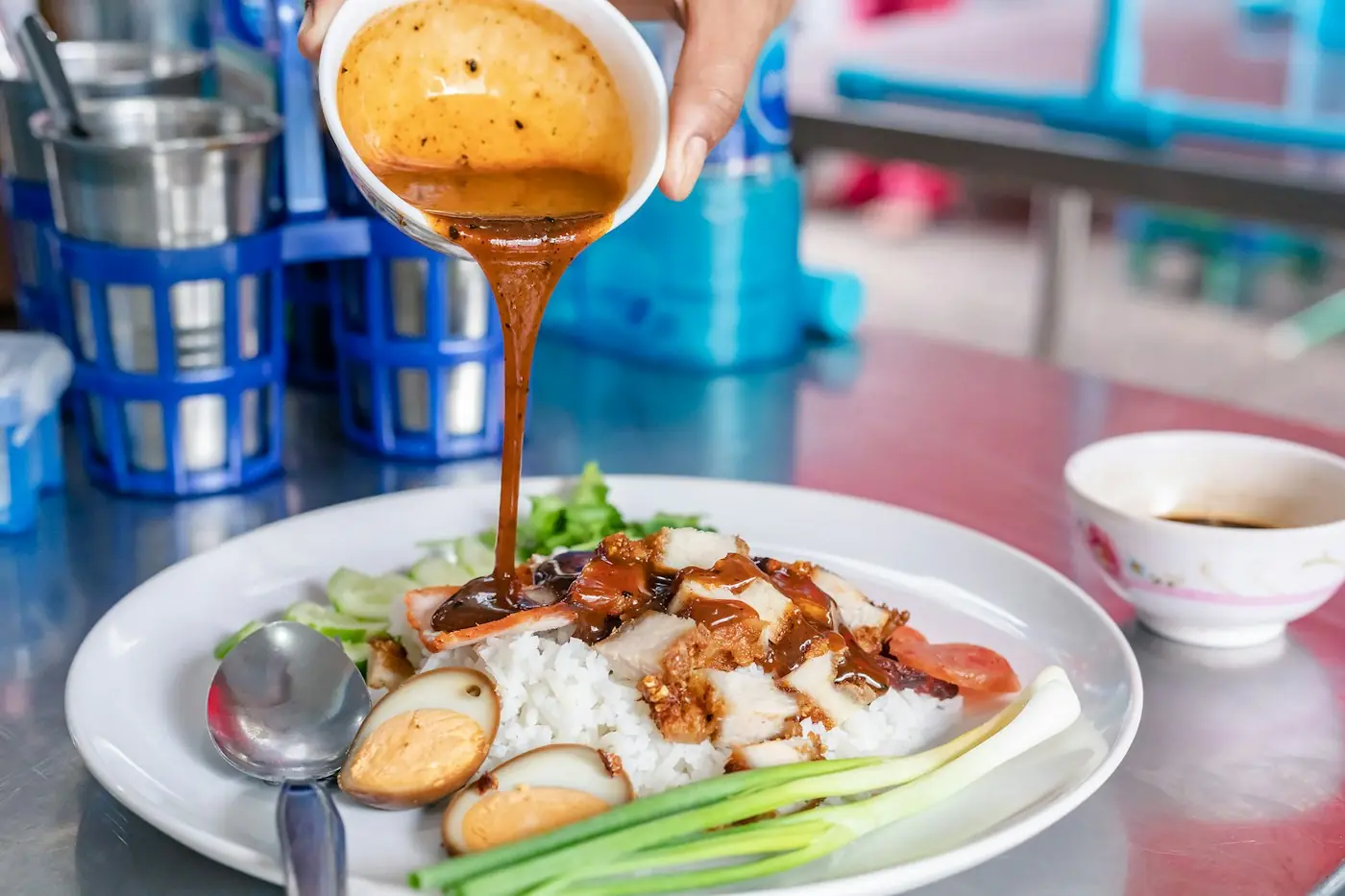 Braised pork on rice with a soft egg and spring onion, sauce being poured over
