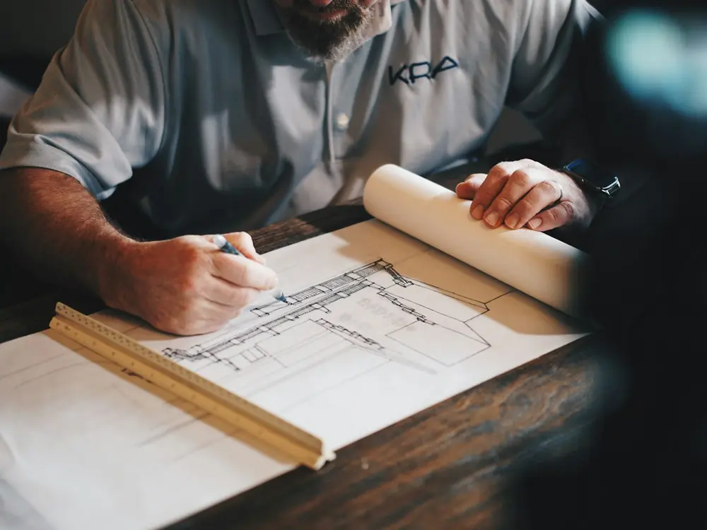 A designer sketching a house elevation on a drawing board with a scale ruler