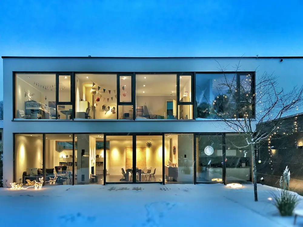 A two-storey rear extension with full-height glazing, lit up on a winter evening