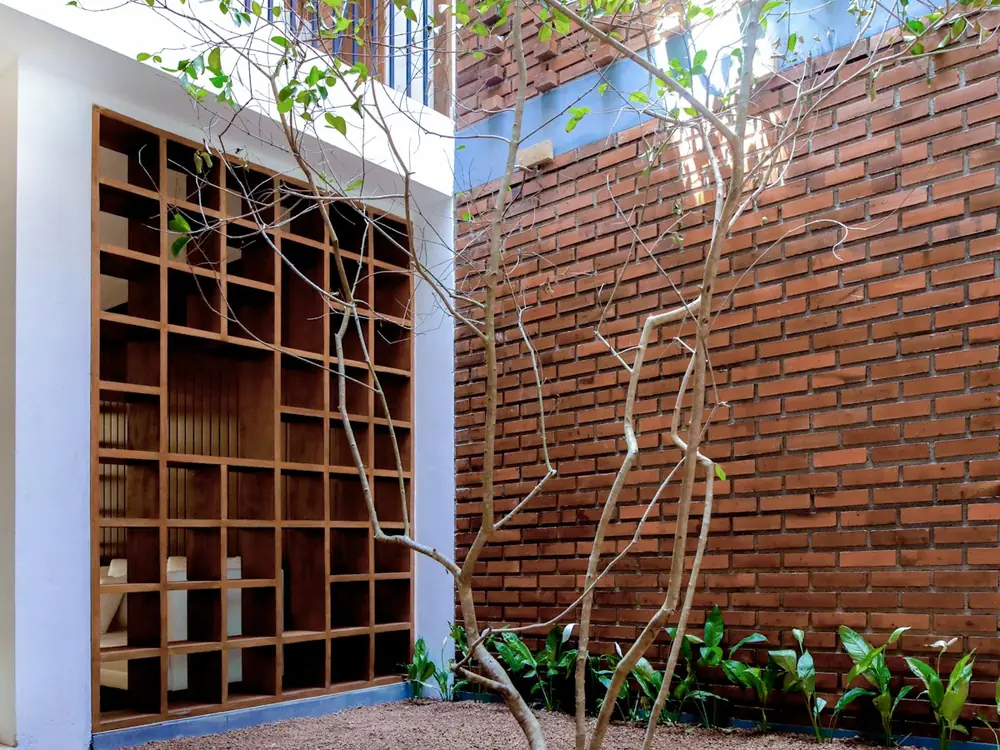 A courtyard between a white wall with timber shelving and a red brick wall
