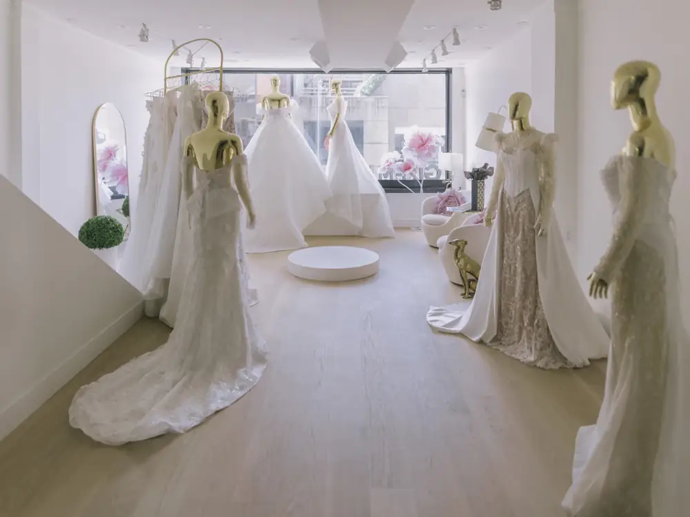Bright bridal salon with gowns on dress forms and a round ottoman