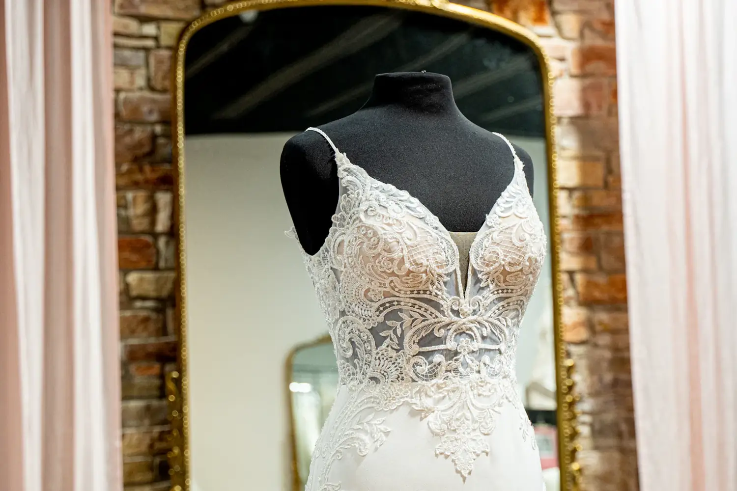 Lace bridal bodice on a dress form in front of a gilded mirror in the atelier