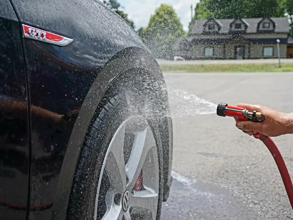 Rinsing the wheel and guard of a dark car with a hose