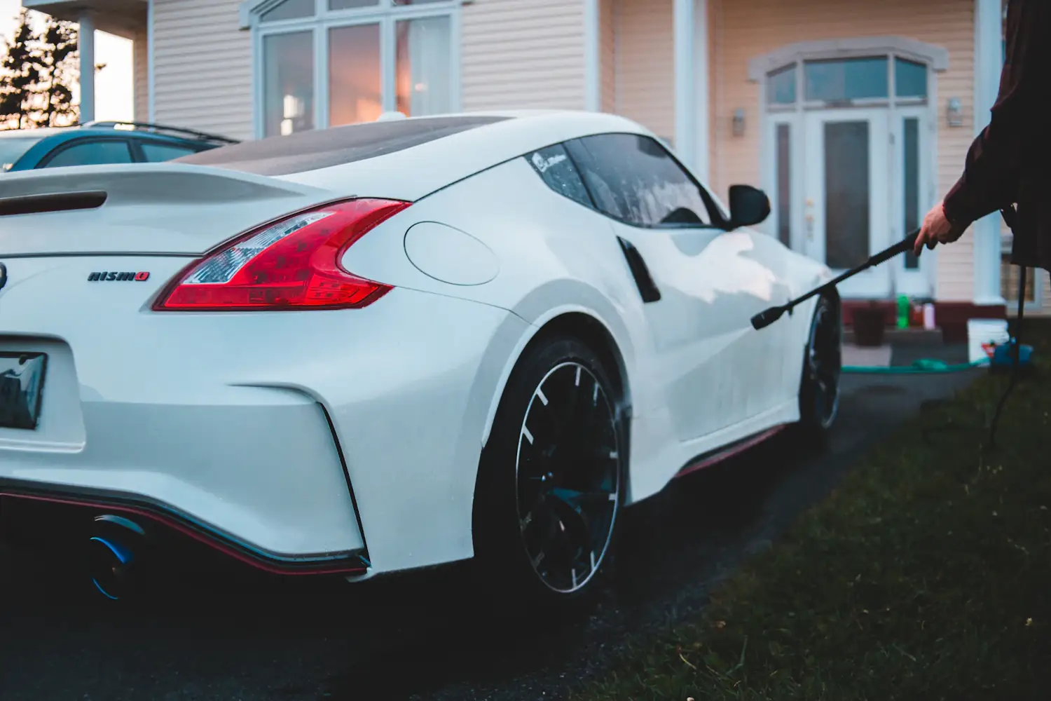 A white sports car being rinsed with a pressure wand in a home driveway