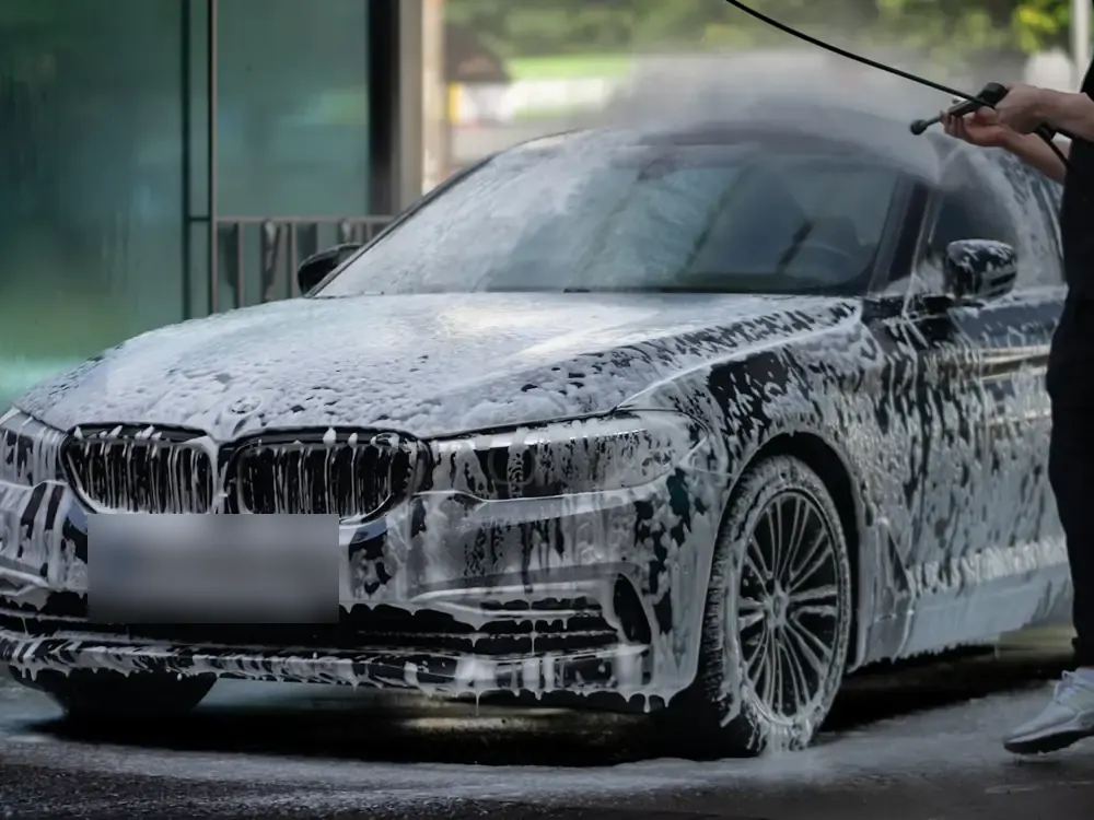 A dark sedan covered in foam being rinsed in a car park