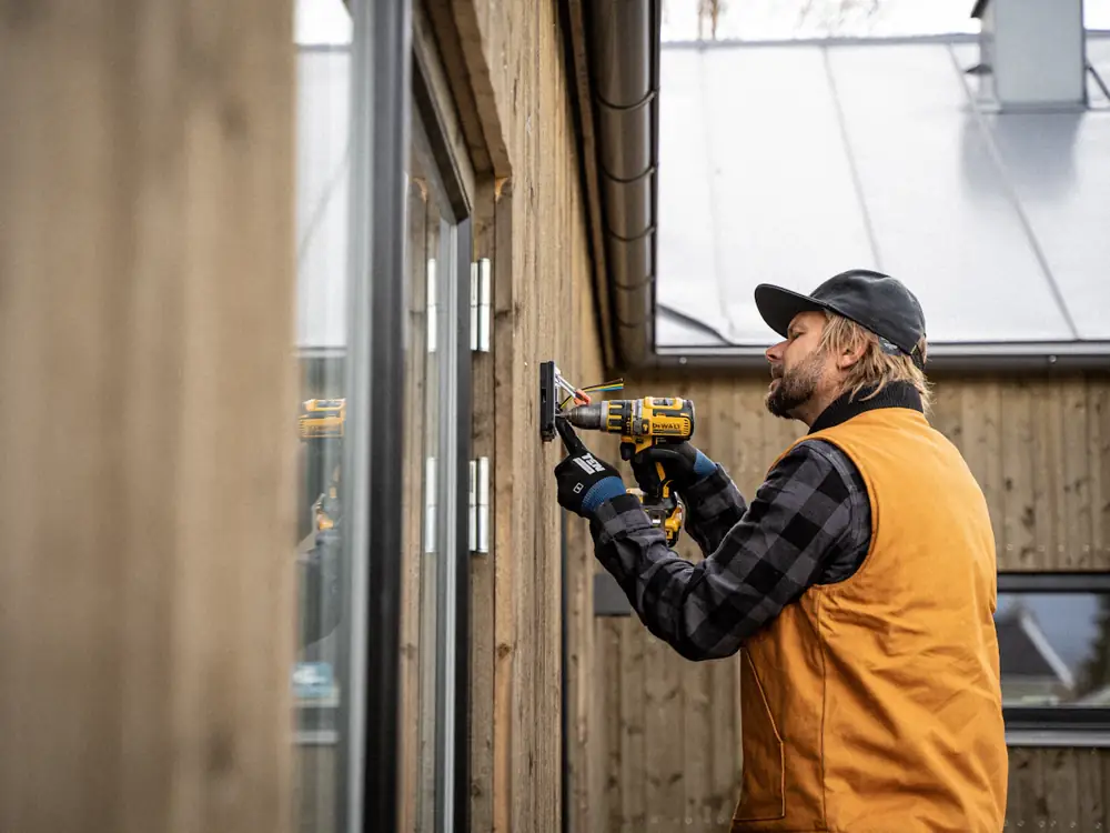 Electrician drilling to mount an outdoor fitting on a timber wall