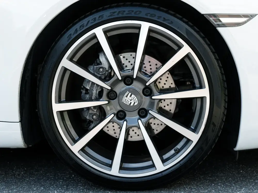 Clean silver alloy wheel with drilled brake disc on a white car