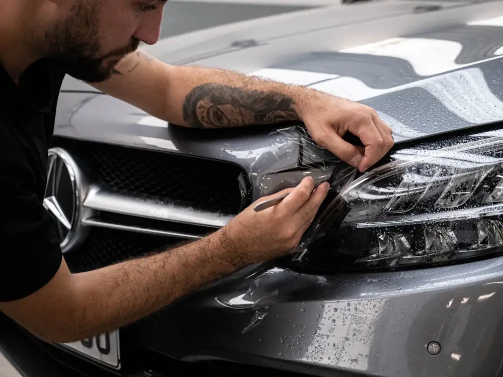 Installer squeegeeing clear paint protection film onto a grey Mercedes bumper