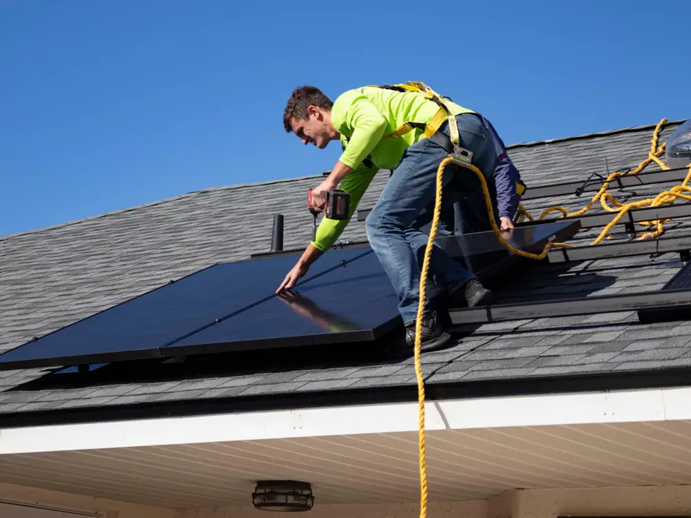 Electrician in a harness fitting solar panels on a tiled roof