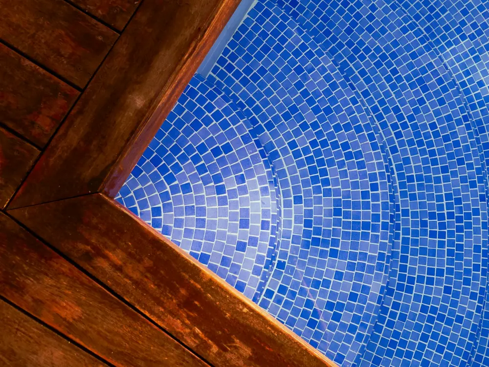 Close-up of blue glass mosaic pool tiles meeting a timber deck edge