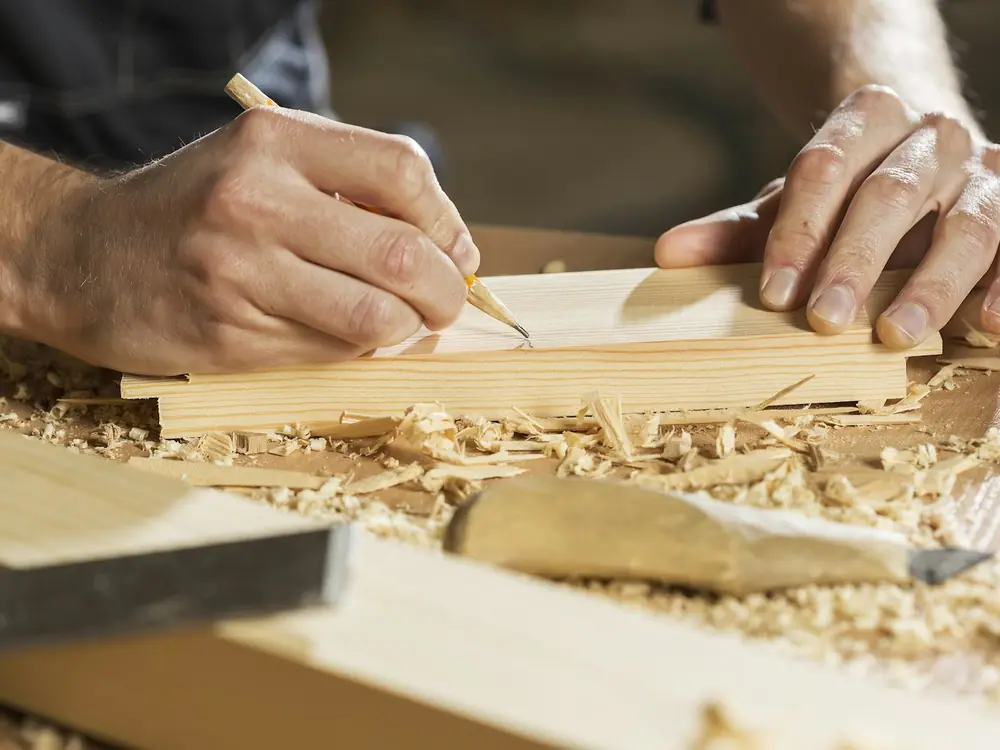 Carpenter marking a length of timber with a pencil among wood shavings