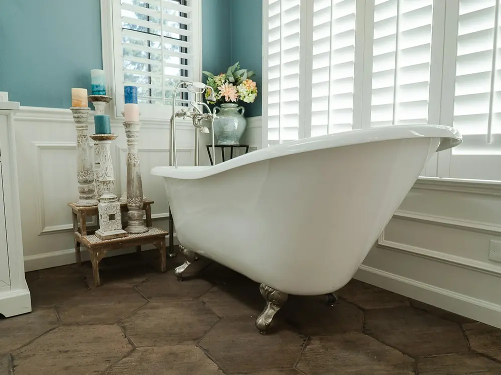 Clawfoot bath under white plantation shutters with wainscoting