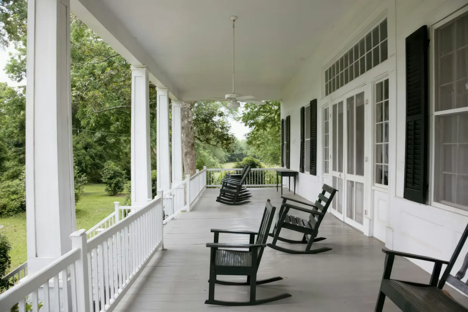 A wide timber verandah with white posts, balustrade and rocking chairs