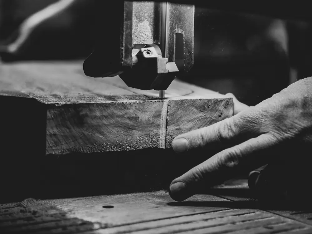 A tiler’s hand guiding a stone tile through a wet saw, in black and white