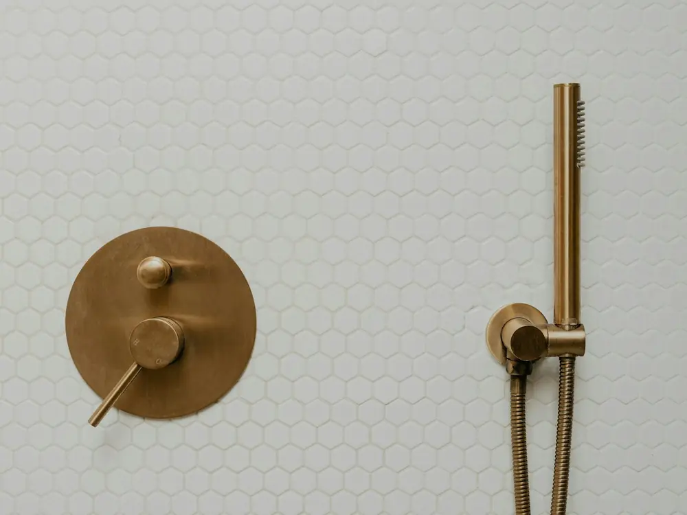 White hexagon mosaic shower wall with brushed brass mixer and hand shower