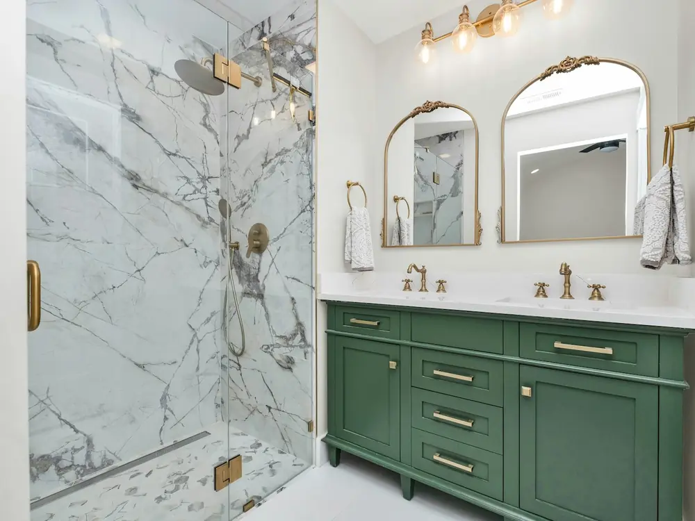 Marble-look tiled shower with frameless glass beside a green double vanity with brass tapware