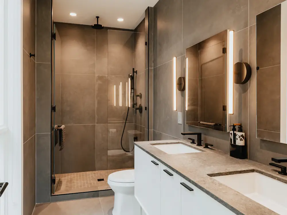 Renovated bathroom with large-format grey tiles, backlit mirrors and a double vanity