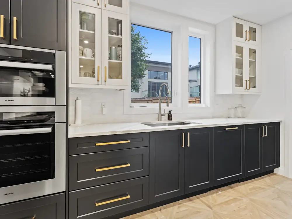 After: charcoal shaker cabinets, brass handles, white stone benchtops and built-in ovens