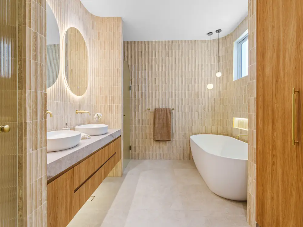 Ensuite with finger tiles, freestanding bath, timber vanity and round lit mirrors