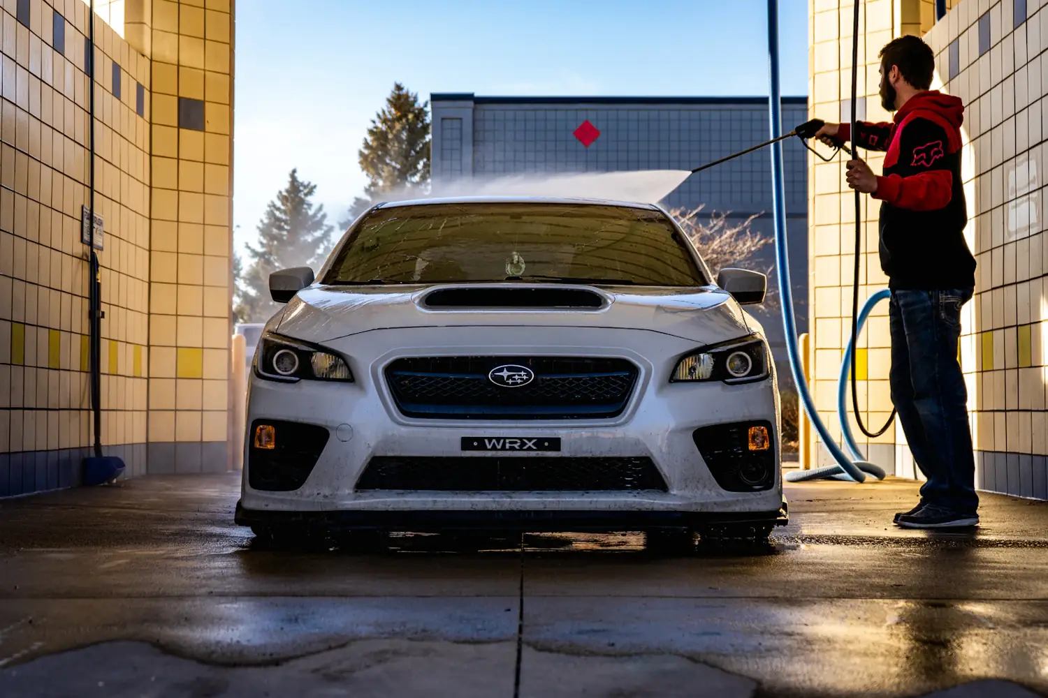 A white Subaru WRX being rinsed in a wash bay