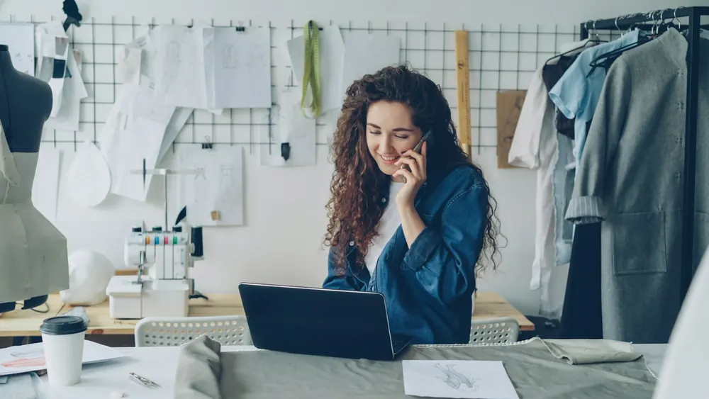 A small-business owner on the phone at her laptop in a design studio