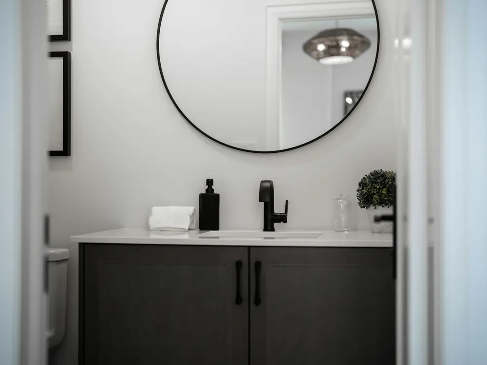 Powder room with a round black-framed mirror and dark vanity